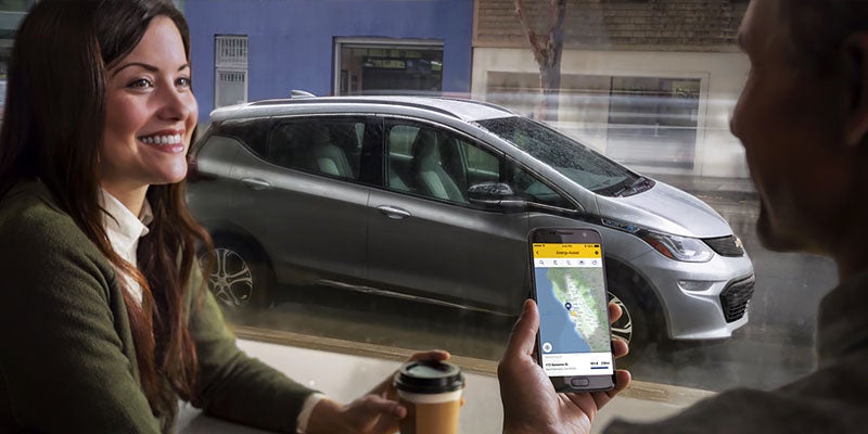 smiling woman and man in a cafe and Chevrolet Bolt EV parked outside